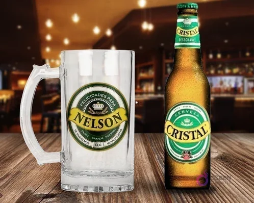 Shopper cervecero de vidrio personalizado con diseño 'Felicidades Papá Nelson' en verde y amarillo, junto a una botella de Cerveza Cristal fría sobre una mesa de madera rústica en un bar.
