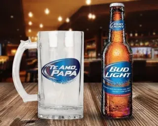 Jarra cervecera transparente con diseño 'Te Amo Papá' en tonos azules y blancos, al estilo de Bud Light, acompañada de una botella de Cerveza Bud Light en una barra de bar difuminada.