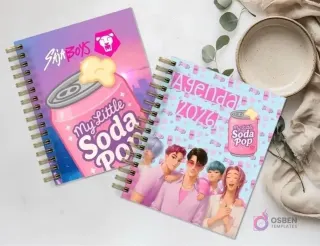 Dos agendas espiraladas 'My Little Soda Pop' / 'Siha Boys' con diseños de personajes masculinos de anime, sobre una superficie de mármol con una planta y un plato vacío.