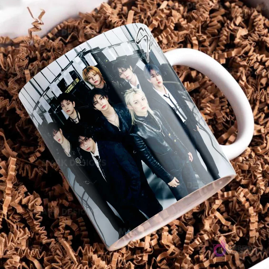Taza blanca con el logo de Stray Kids y otra foto grupal, los miembros con atuendos oscuros de cuero, posando con estilo y seriedad.
