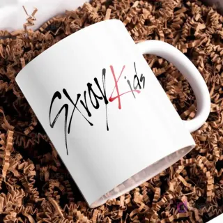 Taza blanca sencilla con el logo distintivo de Stray Kids en letras negras y rojas, fondo liso.