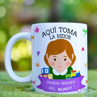 Taza blanca con mensaje 'Aquí Toma La Mejor Educadora' y caricatura de educadora con cabello castaño oscuro, rodeada de elementos de juego y aprendizaje, sobre un fondo bokeh verde