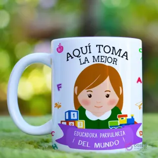 Taza blanca con diseño 'Aquí Toma La Mejor Educadora' y caricatura de educadora con cabello negro, acompañada de bloques, tren y letras de colores, sobre fondo natural difuminado