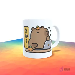 Taza blanca con un capibara trabajando en una laptop, con texto en chino y naranjas a su alrededor.