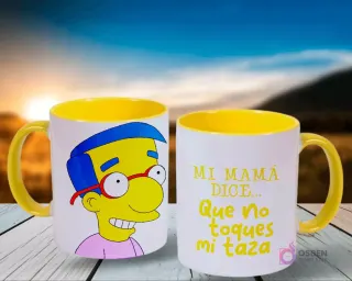 Dos tazas blancas con asas amarillas, mostrando a Milhouse de Los Simpsons en una y la frase 'Mi mamá dice... Que no toques mi taza' en la otra, contra un fondo de atardecer en el campo.