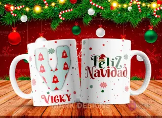 Taza sublimada con la letra V mayúscula en turquesa adornada con campanas, junto al nombre 'VICKY' y al reverso 'Feliz Navidad' con estrellas y copos de nieve.