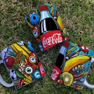 Tres tazas con diseños Pop Art de Coca Cola, botellas y elementos variados en césped