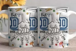 Primer plano de dos tazas blancas sublimadas con el diseño 'Best DAD EVER', destacando el puño de un padre y cuatro manos de niños con nombres como 'Adam', 'Sophia', 'Lucy', 'Max' y herramientas dispersas en el fondo del diseño, sobre una mesa de madera.