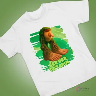 Polera blanca con personaje animado peculiar de nariz grande y pies de raíces verdes, sobre fondo orgánico.