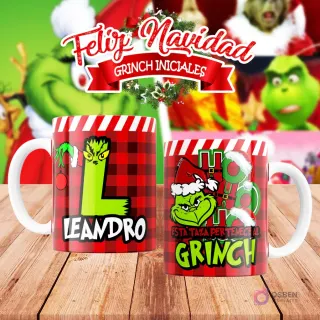 Taza de sublimación del Grinch temática de Navidad con la inicial 'L' y el nombre de ejemplo 'LEANDRO', sobre fondo a cuadros rojo y blanco, junto a otra taza del Grinch con diseño navideño 'Esta Taza Pertenece al Grinch'. El fondo general muestra personajes del Grinch en Navidad.