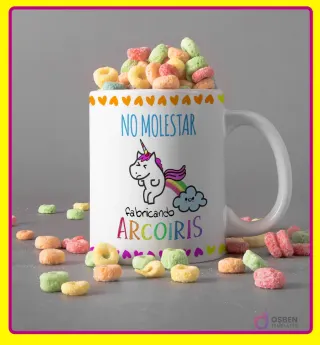 Taza blanca con diseño de unicornio haciendo caca de arcoíris y frase 'NO MOLESTAR fabricando ARCOIRIS', con cereales de colores y borde amarillo.