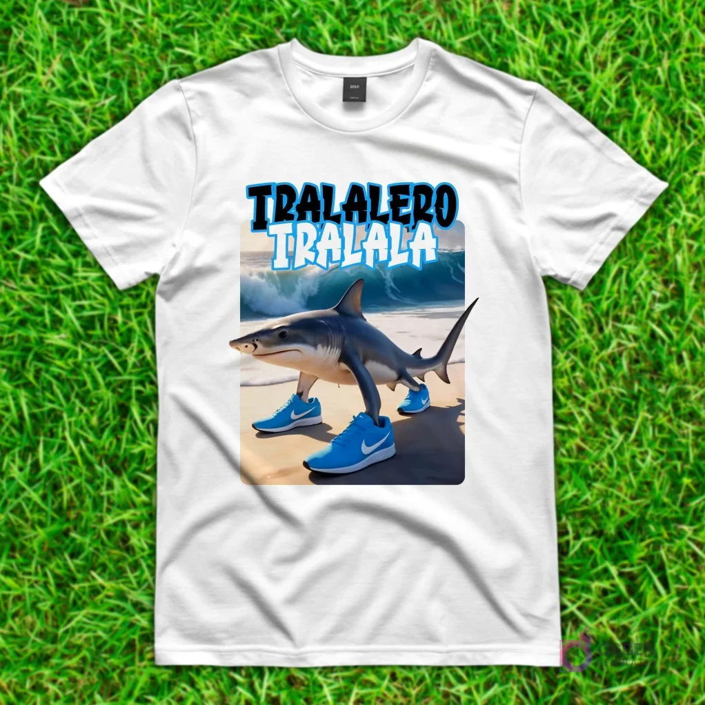 Camiseta blanca con diseño de 'Tralalero Tralala', un tiburón con piernas humanas y zapatillas deportivas azules, caminando en una playa con olas.
