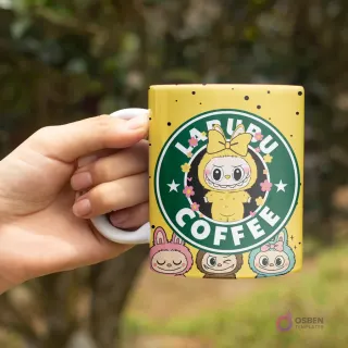Mano sosteniendo una taza amarilla con asa blanca, diseño 'LABUBU COFFEE' con un Labubu amarillo pensativo y florecitas de colores de fondo.