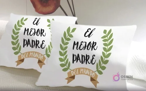 Cojines blancos con un diseño sublimado que reza 'El mejor padre del mundo' enmarcado por laureles verdes y una cinta marrón, ideal para reconocer a papá.