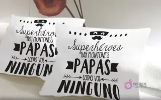Cojines blancos sublimados con la frase 'Superhéroes hay montones Papas como vos NINGUNO' en negro, con un icono de bigote y máscara, un mensaje único y emotivo.