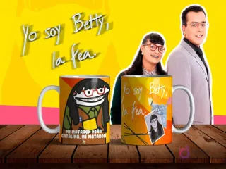 Dos tazas de sublimación con diseños de Flork Betty la Fea, una con la frase 'ME MATARON DOÑA CATALINA, ME MATARON :(' y otra con Betty Pinzón original, sobre mesa de madera con fondo amarillo y personajes de la telenovela.