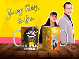 Dos tazas de sublimación con diseños de Flork Betty la Fea, una con la frase 'MI BELLEZA ES NATURAL' y otra con Betty Pinzón original, sobre mesa de madera con fondo amarillo y personajes de la telenovela.