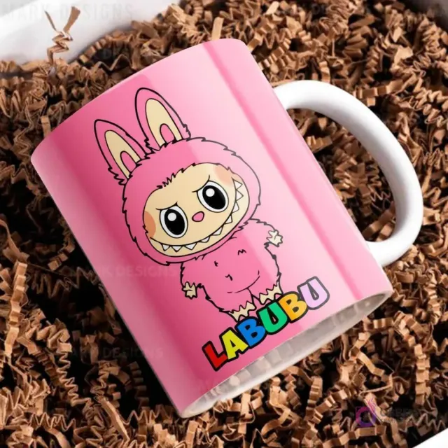 Taza de cerámica rosa con diseño del personaje Labubu de traje peludo rosa, con el nombre Labubu en letras coloridas, sobre papel picado marrón.