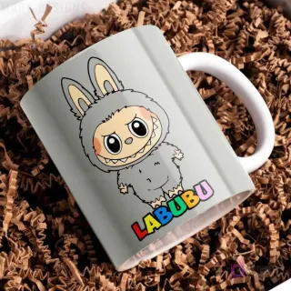Taza de cerámica gris claro con diseño del personaje Labubu de traje peludo gris, con el nombre Labubu en letras coloridas, sobre papel picado marrón.