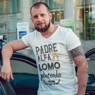 Hombre con barba vistiendo camiseta blanca sublimada con el diseño 'PADRE ALFA LOMO plateado desde 2018' y botellas de cerveza, mostrando un mockup real.
