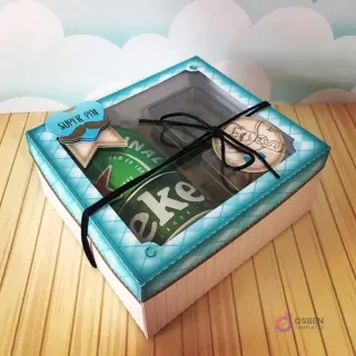 Caja cuadrada cerrada con ventana, conteniendo una cerveza Heineken y dos pequeños contenedores de snacks, decorada con diseño azul a cuadros y etiqueta 'Super Pai' para el Día del Padre.