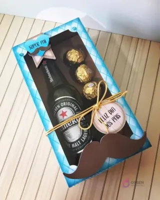 Caja rectangular cerrada con ventana, con una botella de cerveza Heineken y tres chocolates Ferrero Rocher, decorada con un gran bigote y etiqueta 'Feliz Día dos Pais'.