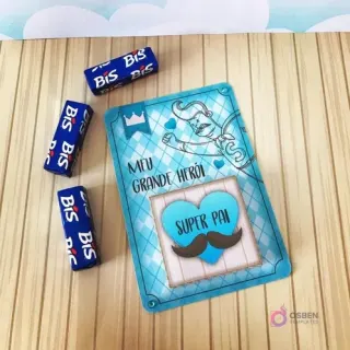 Tarjeta decorativa 'Meu Grande Herói Super Pai' con diseño de bigotes y coronas, junto a tres chocolates Bis envueltos, ideal para complementar un Candy Bar del Día del Padre.