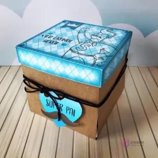 Caja explosiva cerrada en color kraft con tapa decorada en tonos azules y blancos, atada con lazo negro y etiqueta 'Super Pai', diseño para el Día del Padre.