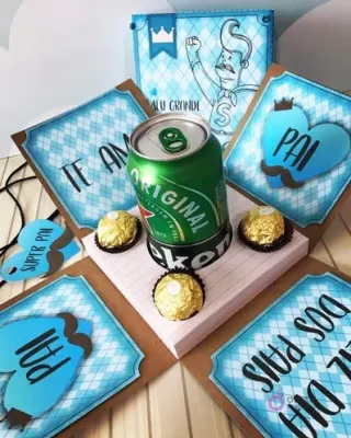 Caja explosiva abierta mostrando una lata de cerveza Heineken, tres chocolates Ferrero Rocher y cuatro paneles con mensajes 'Te Amo' y 'Pai', diseño digital para el Día del Padre.