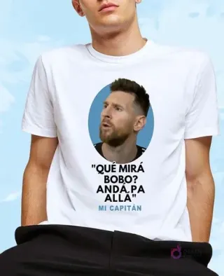 Hombre con camiseta blanca estampada con la frase "Qué Mirás Bobo" y retrato ovalado de Lionel Messi mirando a la derecha sobre fondo celeste, perfecto para crear merchandising.