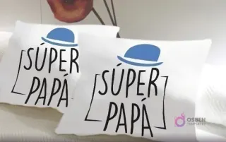 Dos cojines blancos personalizados con el diseño 'SÚPER PAPÁ' en tipografía moderna y un sombrero azul.