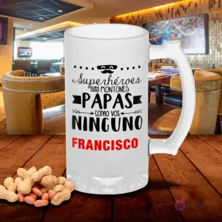 Jarra cervecera esmerilada con diseño 'Superhéroes hay montones Papas como vos ninguno' con bigote y antifaz, sobre mesa rústica con cacahuetes, fondo de bar. Plantilla Día del Padre original.