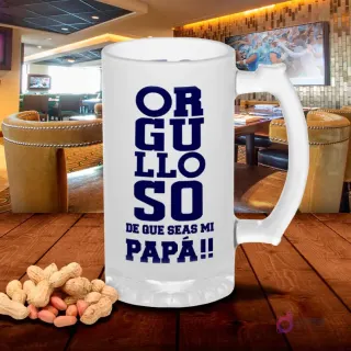 Jarra de cerveza esmerilada con diseño 'ORGULLOSO DE QUE SEAS MI PAPÁ!!' en letras grandes azules, sobre mesa de madera con cacahuetes, fondo de bar. Plantilla sublimación Padre Orgulloso.