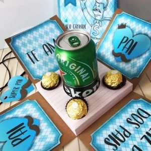Caja explosiva abierta mostrando una lata de cerveza Heineken, tres chocolates Ferrero Rocher y cuatro paneles con mensajes 'Te Amo' y 'Pai', diseño digital para el Día del Padre.