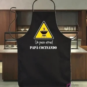 Delantal negro sublimado con diseño vectorial de humor 'Un paso atrás! Papá Cocinando' y señal de advertencia de parrilla.