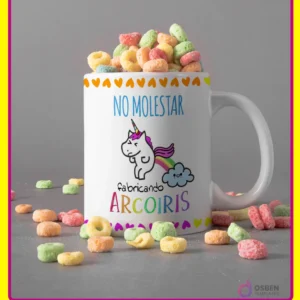 Taza blanca con diseño de unicornio haciendo caca de arcoíris y frase 'NO MOLESTAR fabricando ARCOIRIS', con cereales de colores y borde amarillo.