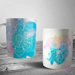 Dos tazas blancas con un diseño de mandala de contorno blanco sobre un fondo de suaves manchas de acuarela azul y morado, creando un efecto etéreo.