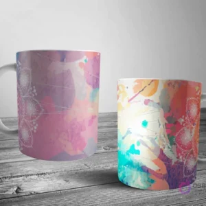 Dos tazas blancas con un diseño de mandala de contorno blanco parcialmente oculto por salpicaduras abstractas de acuarela en rosa, morado, naranja y azul.