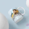 Mockup de taza blanca para sublimación con diseño de Lionel Messi y la frase '¿Qué Mirás Bobo? Andá Pa' Allá'. El diseño incluye detalles de la bandera argentina y el sol, sobre un fondo azul claro con dos esferas blancas. La taza está flotando en un ángulo dinámico.