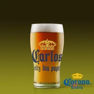 Vaso de cerveza con etiqueta personalizada 'Carlos Feliz día papito' inspirada en Cerveza Corona, fondo verde oscuro.