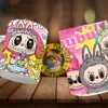Dos tazas Labubu flotantes. Taza izquierda con Labubu con orejas de conejo rosadas y texto 'Hello My Labubu'. Taza derecha con tres personajes estilo Labubu, uno gris, uno rosa, y texto 'Bububu'. Fondo de madera.