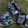 Tres tazas blancas con diseños de Stitch Black Galaxia sobre césped verde, mostrando a Stitch de pie con brazos extendidos y fondo cósmico con "Ohana".