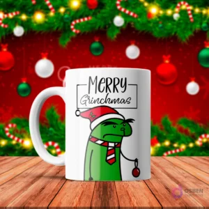 Taza de sublimación blanca con Flork verde disfrazado de Grinch con gorro de Santa y corbata, sosteniendo un adorno rojo, texto 'Merry Grinchmas' con fondo navideño rojo.