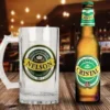 Shopper cervecero de vidrio personalizado con diseño 'Felicidades Papá Nelson' en verde y amarillo, junto a una botella de Cerveza Cristal fría sobre una mesa de madera rústica en un bar.