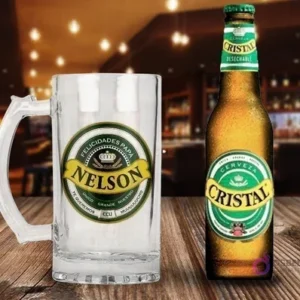 Shopper cervecero de vidrio personalizado con diseño 'Felicidades Papá Nelson' en verde y amarillo, junto a una botella de Cerveza Cristal fría sobre una mesa de madera rústica en un bar.