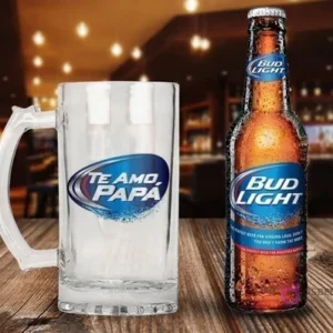 Jarra cervecera transparente con diseño 'Te Amo Papá' en tonos azules y blancos, al estilo de Bud Light, acompañada de una botella de Cerveza Bud Light en una barra de bar difuminada.