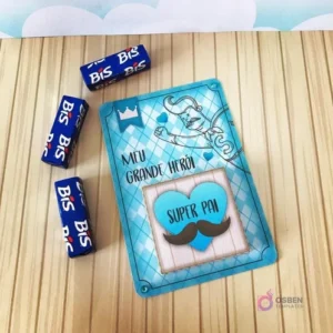 Tarjeta decorativa 'Meu Grande Herói Super Pai' con diseño de bigotes y coronas, junto a tres chocolates Bis envueltos, ideal para complementar un Candy Bar del Día del Padre.