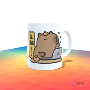 Taza blanca con un capibara trabajando en una laptop, con texto en chino y naranjas a su alrededor.