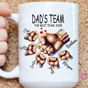 Mano sosteniendo una taza grande de sublimación con el diseño 'Dad's Team The Best Team Ever' y siete puños personalizados con nombres, resaltando la capacidad de añadir más miembros de la familia.