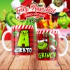 Taza de sublimación del Grinch temática de Navidad con la inicial 'A' y el nombre de ejemplo 'ALBERTO', sobre fondo a cuadros rojo y blanco, junto a otra taza del Grinch con diseño navideño 'Esta Taza Pertenece al Grinch'. El fondo general muestra personajes del Grinch en Navidad.